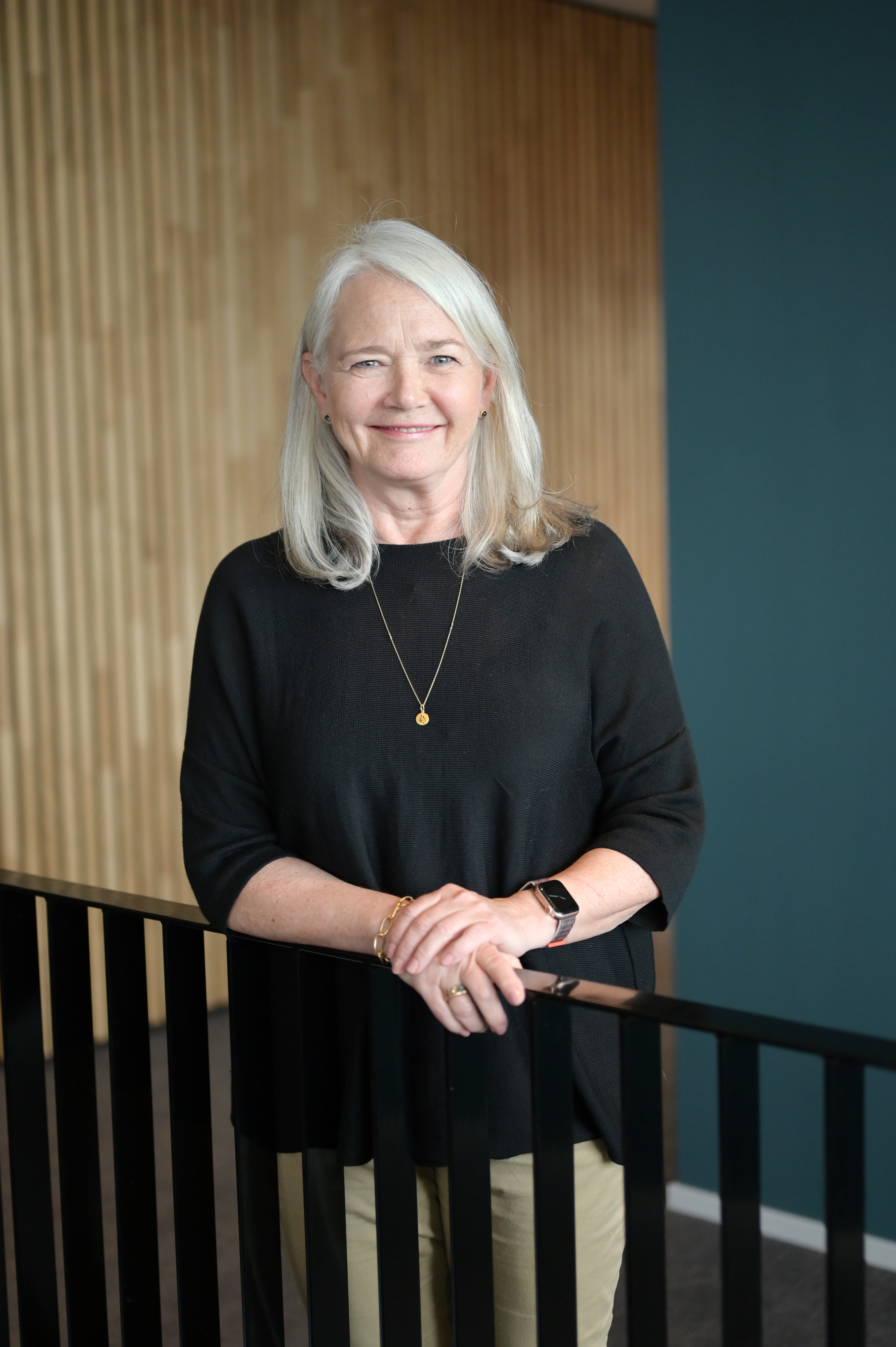 dame som står ved rekkverk inne på et kontor smiler