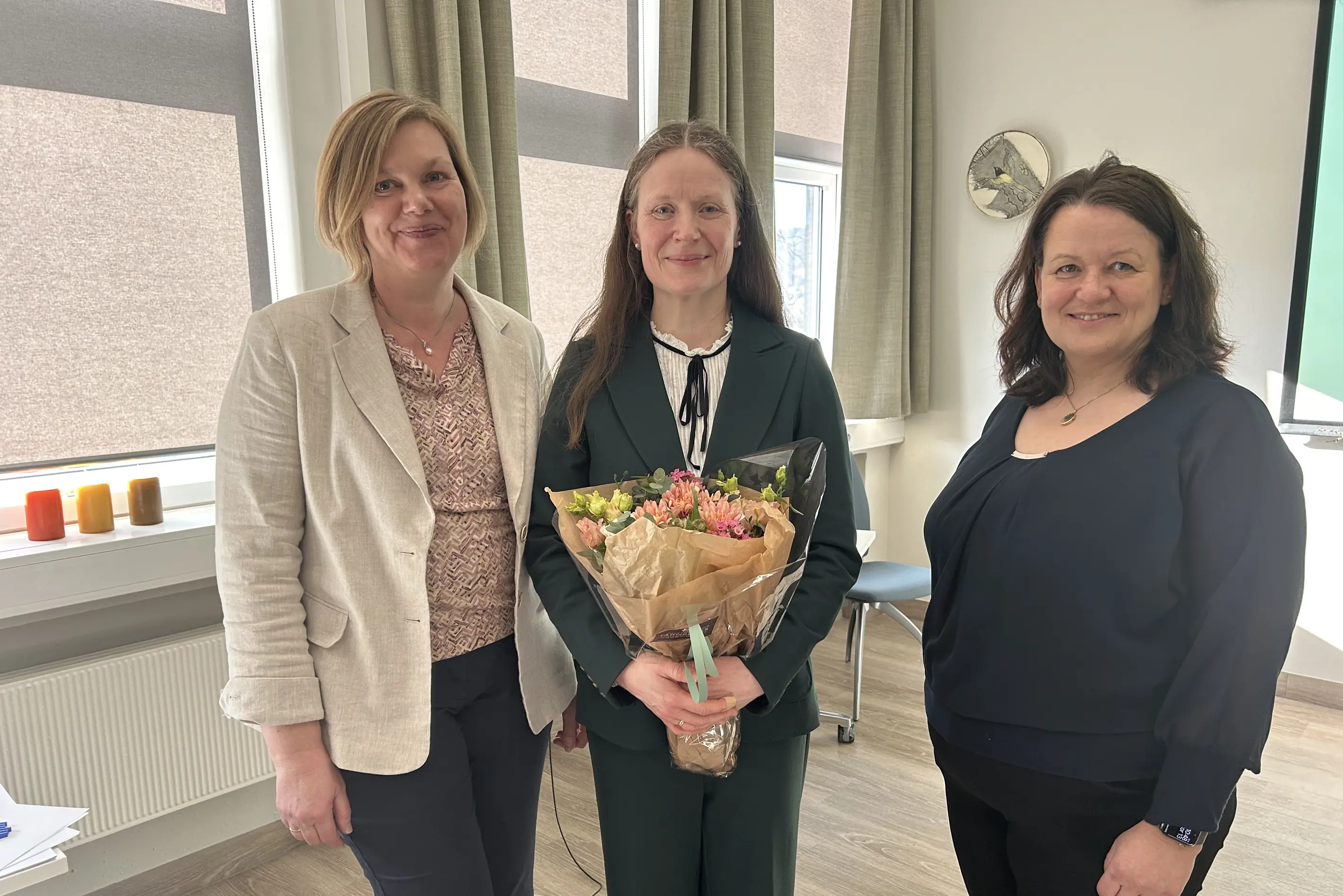 To kvinner flankerer ei kvinne som held ein bukett