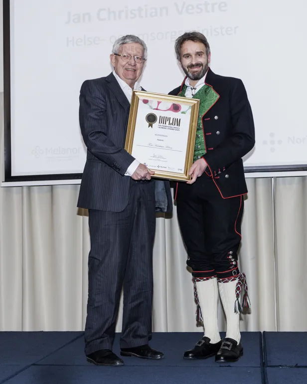 En person som holder et sertifikat ved siden av en person som holder en plakett