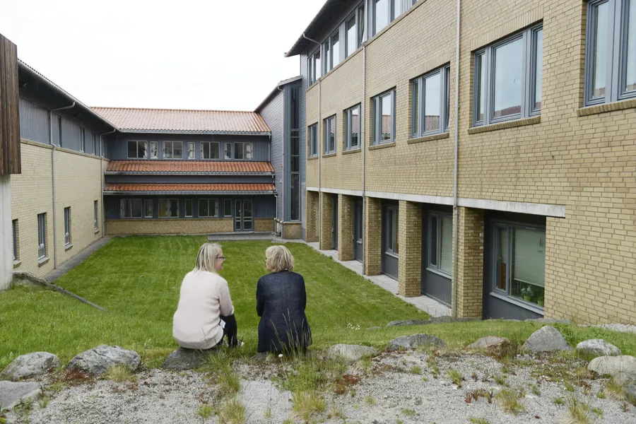 To personer sitter i utendørs atrium og snakker. Foto.