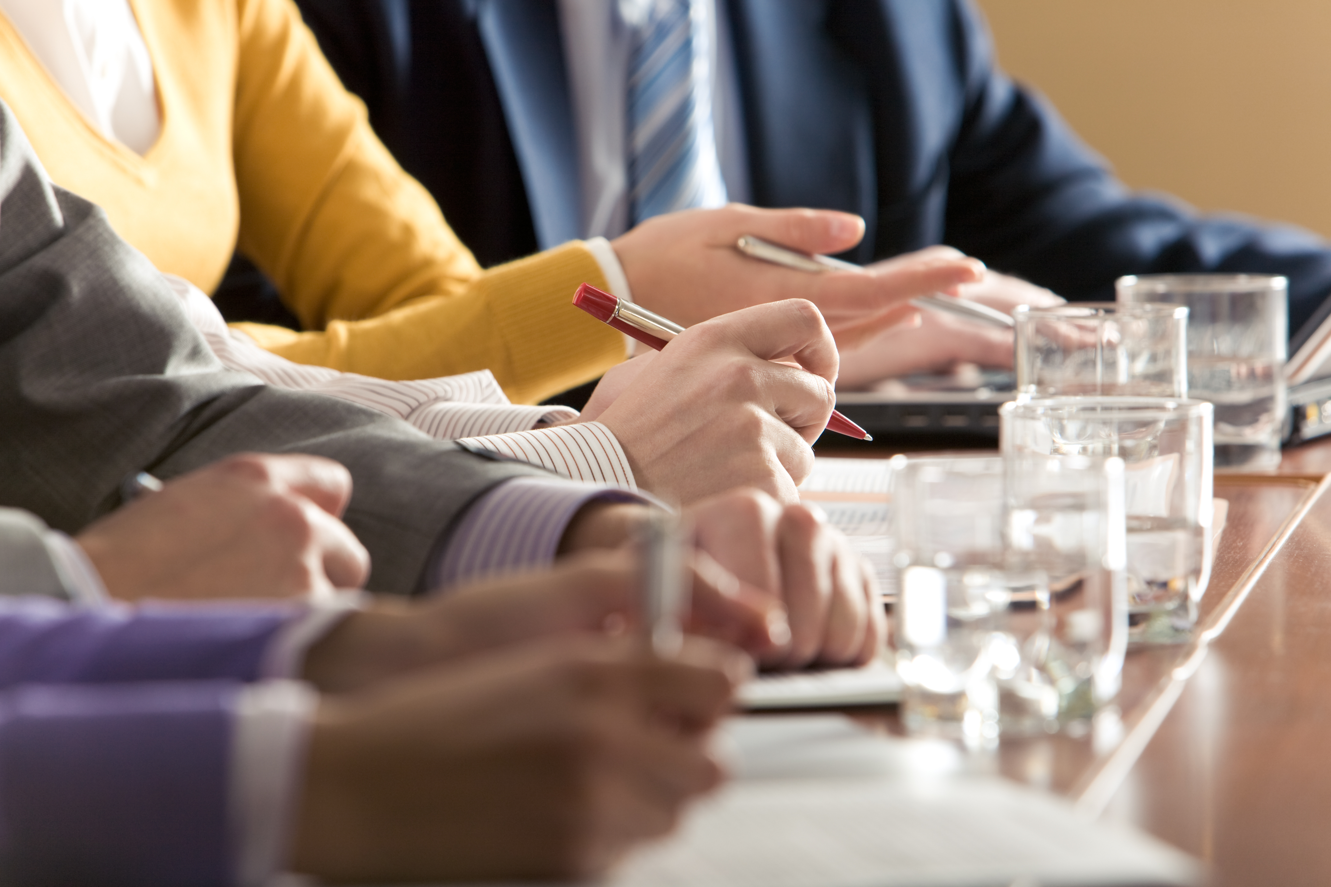 Flere personer sitter ved et bord og skriver og snakker. Foto.