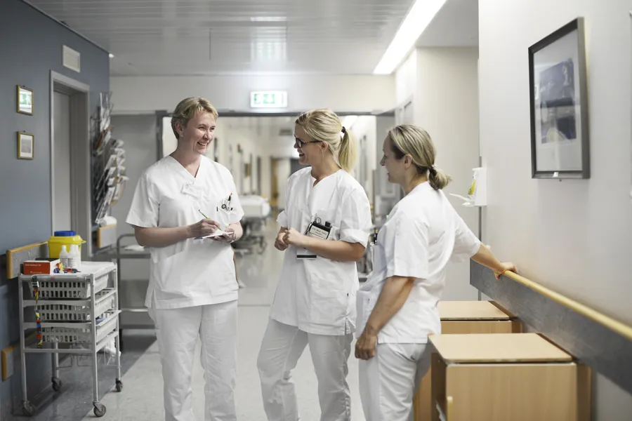Tre pleiarar står i ein sjukehuskorridor og pratar