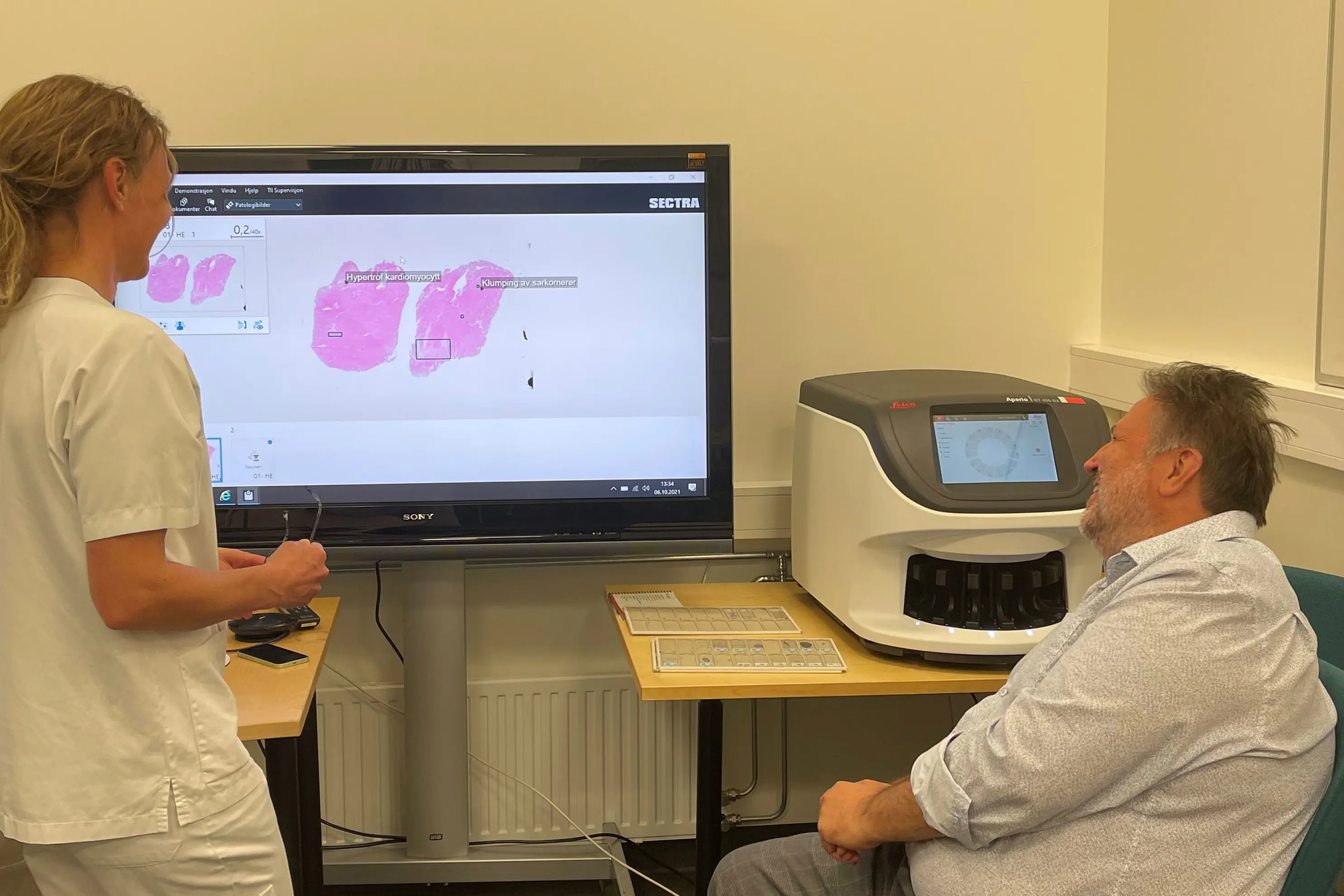 Kvinne og mann ser på bilete av patologisk prøve, på ein skjerm.