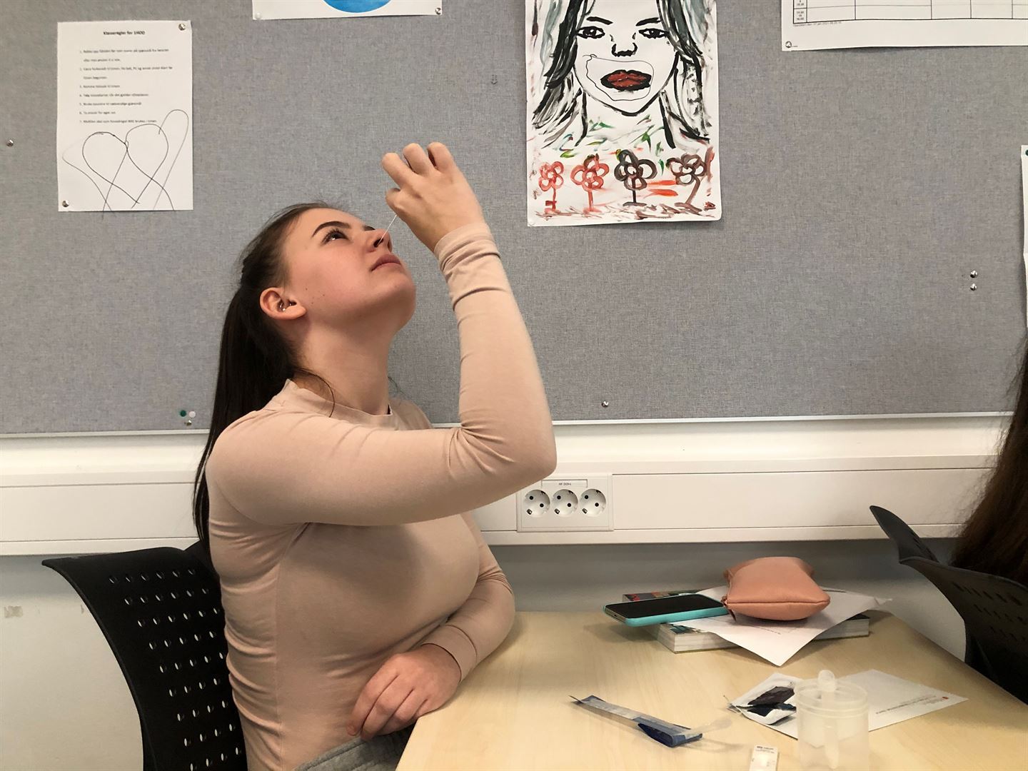 Elev ved pult i klasserom testar seg sjølv for koronavirus med å putta ein vattpinne i nasen. 