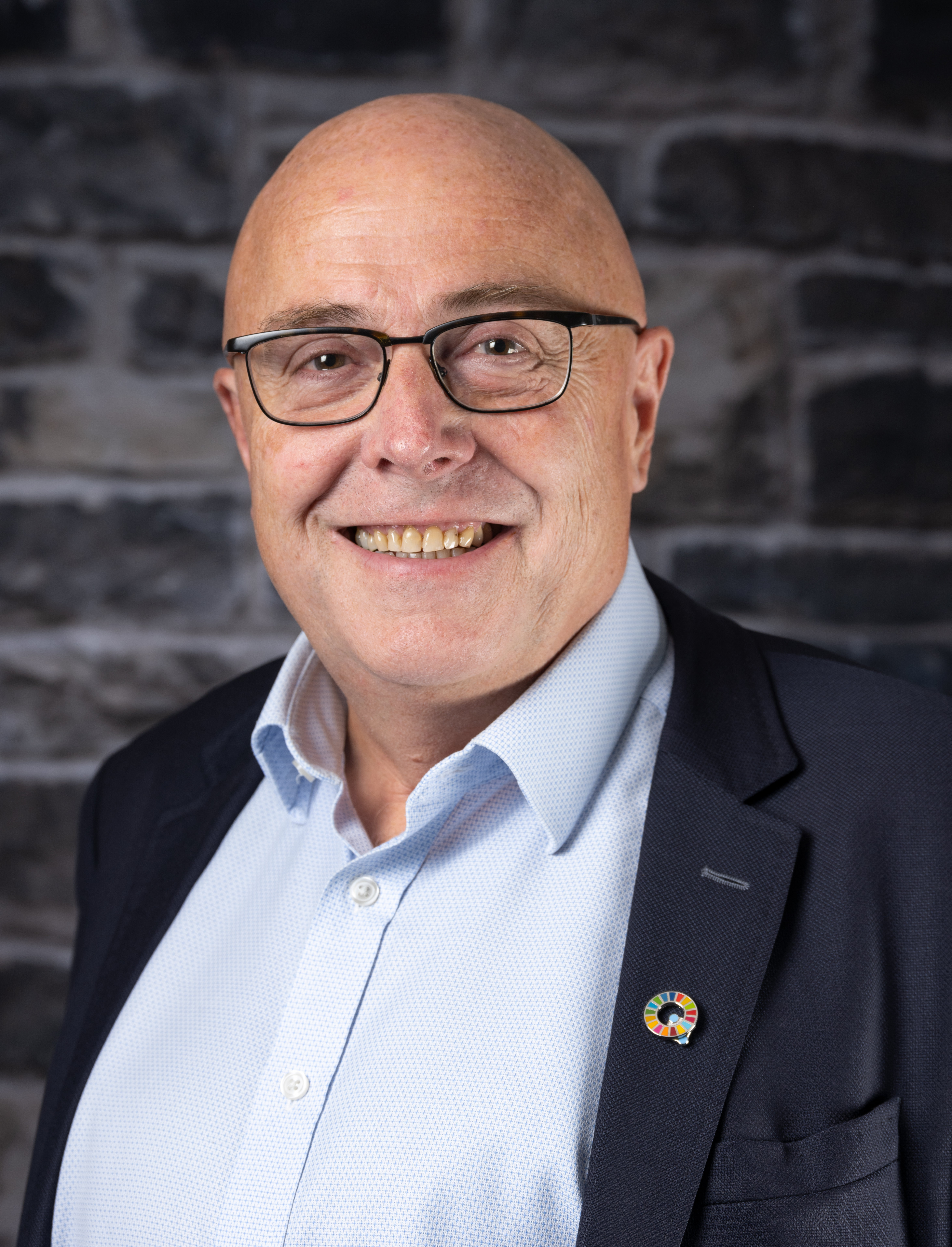 Mann med briller og dress smiler. Foto.