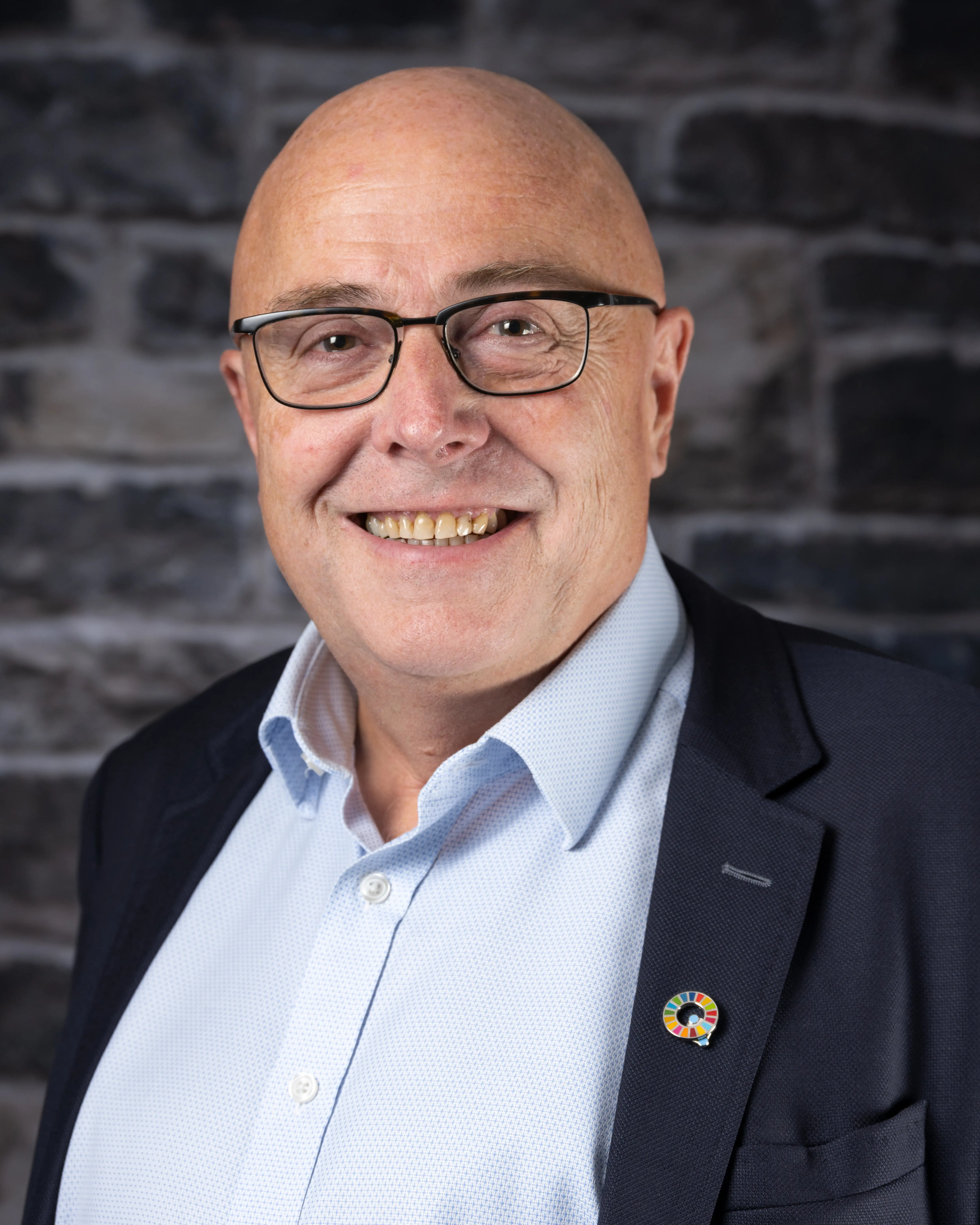 Mann med briller og dress smiler. Foto.