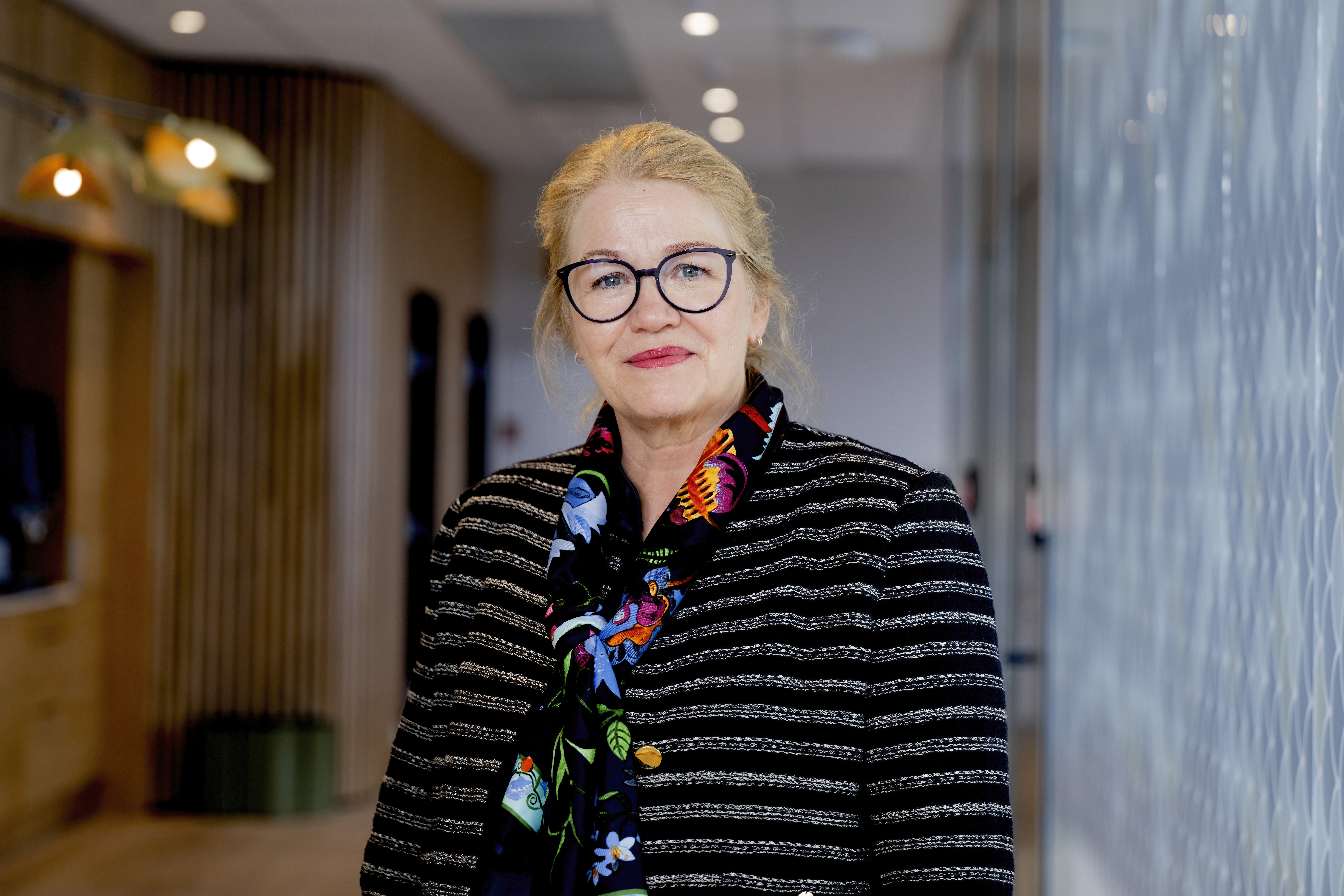 Dame ser mot kamera, står i en gang