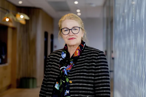 Dame ser mot kamera, står i en gang