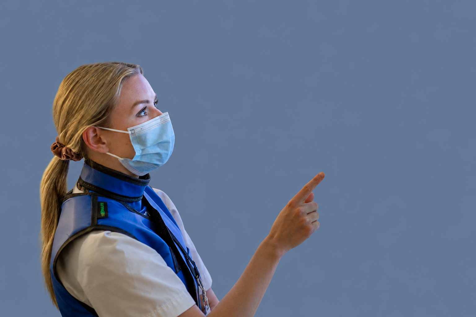 En lege med munnbind og radiologivest som peker. Blågrå bakgrunn