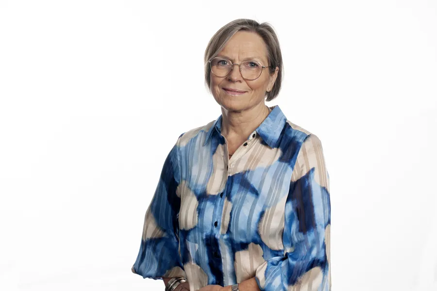 Kvinne med briller og blå og hvit bluse. Lett smil. Foto.