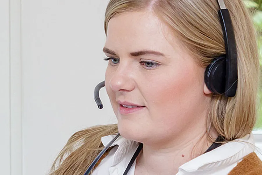 Kvinne med headset foran PC. Foto.