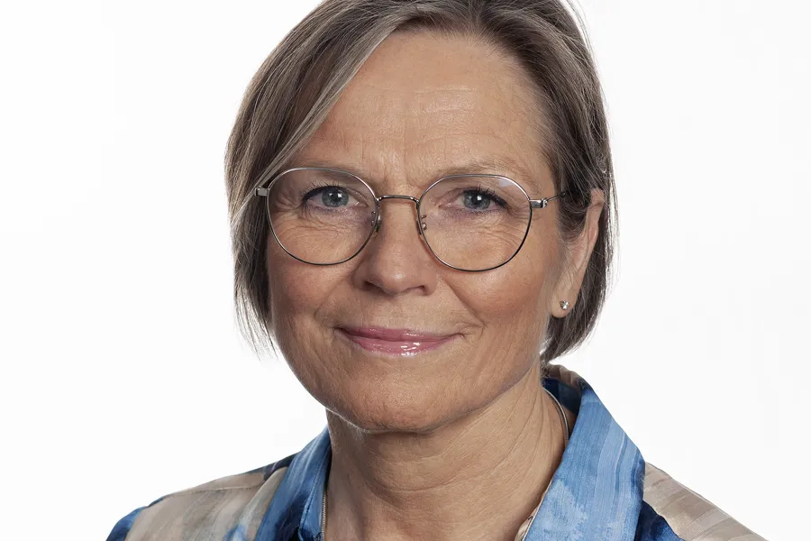 Kvinne i hvit og blå bluse, briller. Foto.