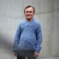 Mann med blå genser står i trapp og ser mot kamera